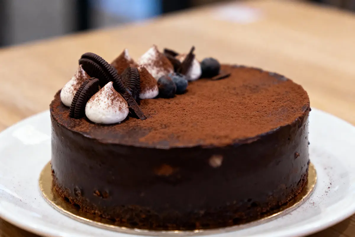 Gâteau au chocolat décoré de crème, biscuits noirs, et baies sur assiette blanche.