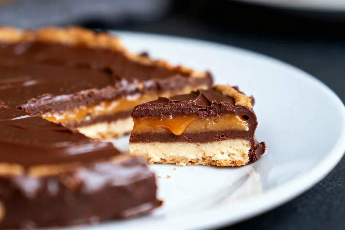 Une tarte au chocolat avec couches de caramel et pâte croquante sur une assiette blanche.