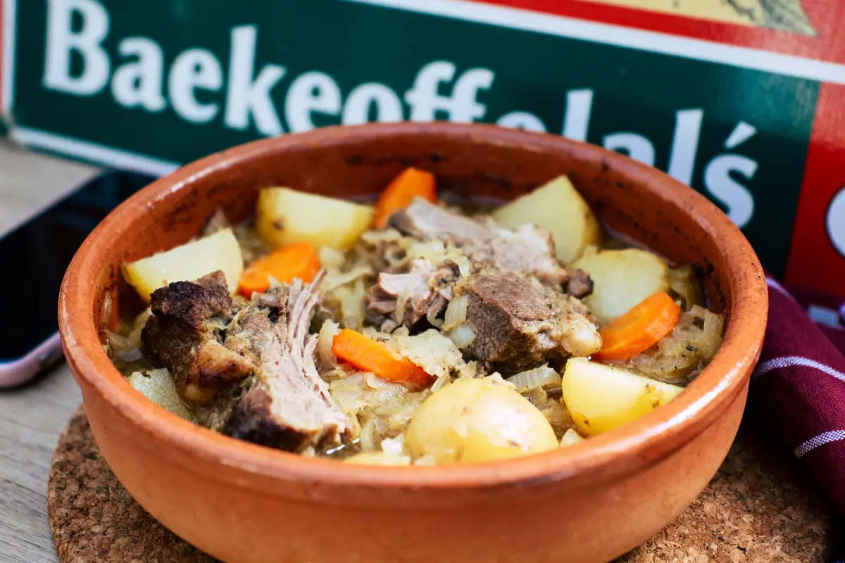 Plat de Baekeoffe alsacien avec viande, pommes de terre, carottes, dans un plat en terre cuite sur table.