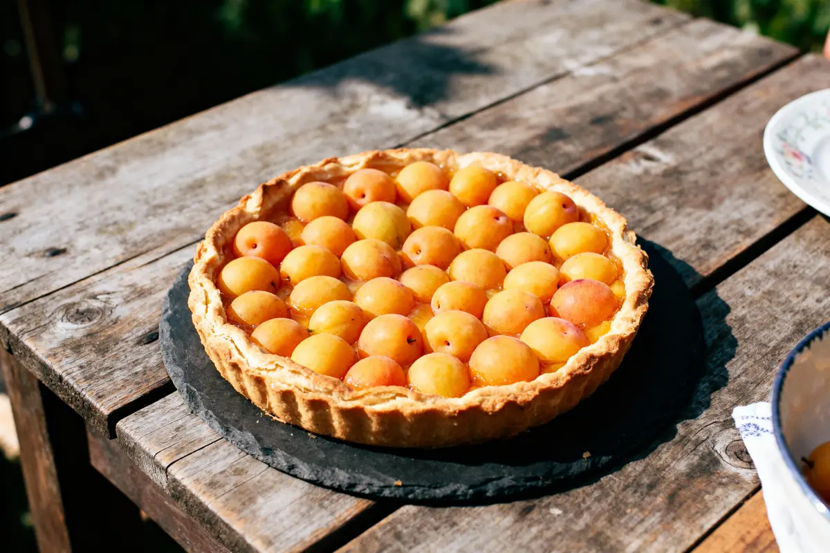 Tarte aux mirabelles dorées sur table en bois, éclairée par le soleil.