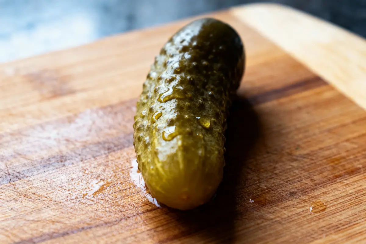 Cornichon mariné sur une planche à découper en bois, avec des gouttes de liquide.