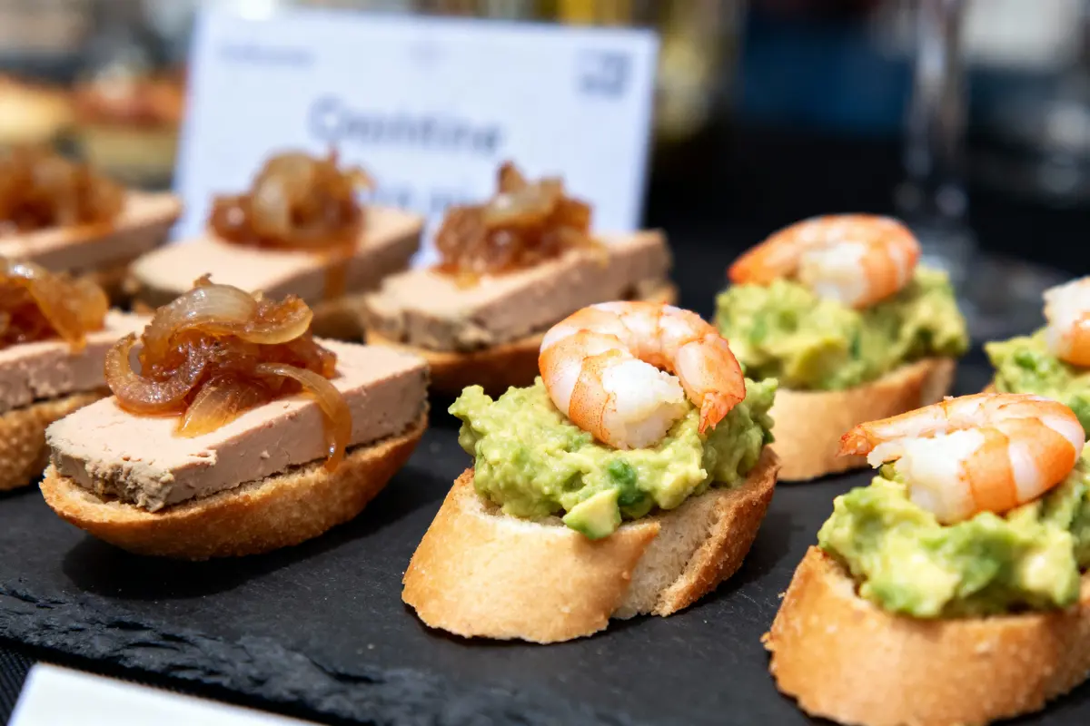 Canapés garnis de crevettes sur avocat et de foie gras avec oignons, présentés sur une ardoise.