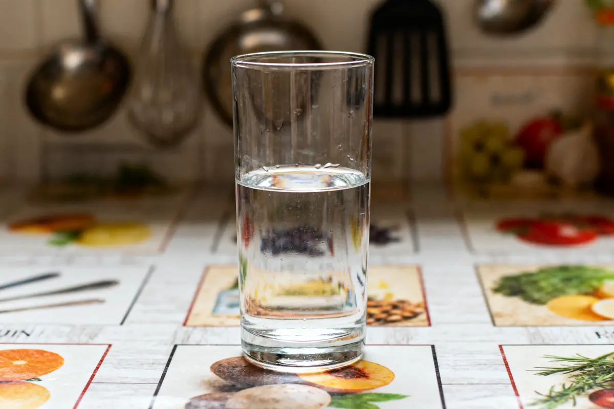 Verre d'eau sur une table de cuisine avec motifs colorés, ustensiles flous en arrière-plan.