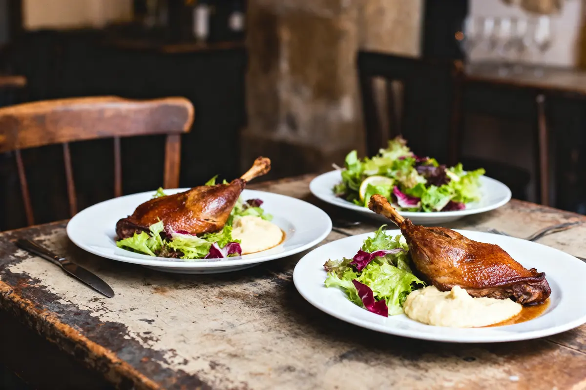 Trois assiettes de canard confit, purée, et salade sur table en bois rustique.