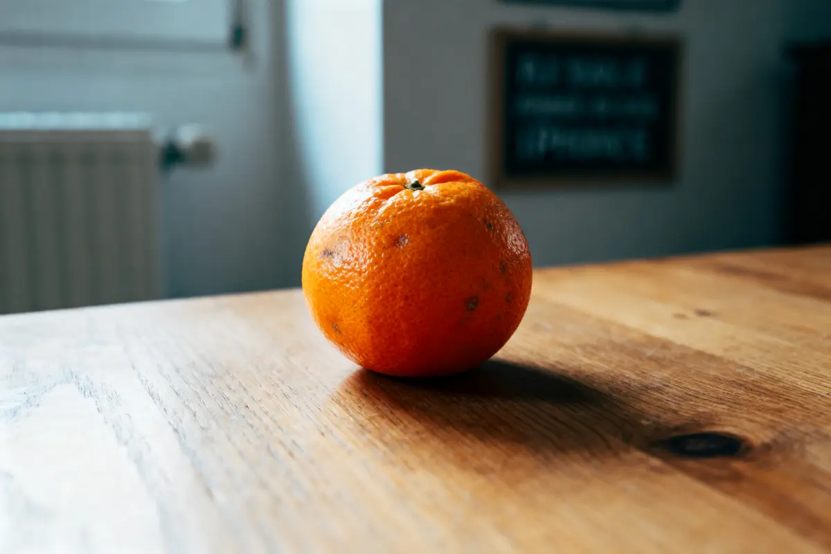 Une orange posée sur une table en bois, lumière naturelle douce.