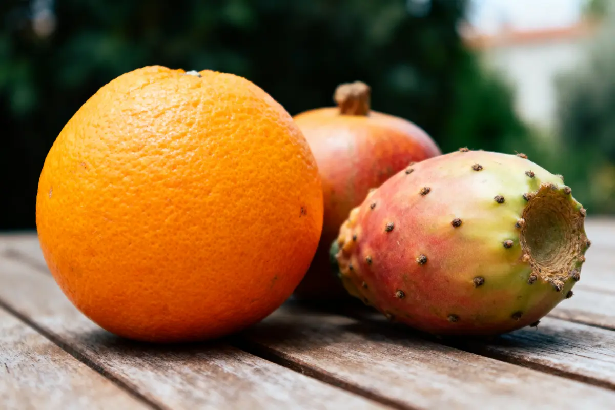 Orange, grenade, et figue de Barbarie sur table en bois, arrière-plan flou nature.