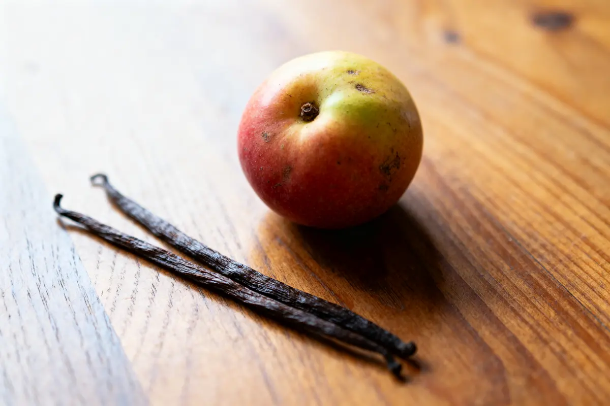 Pomme rouge et jaune et gousses de vanille sur une table en bois.