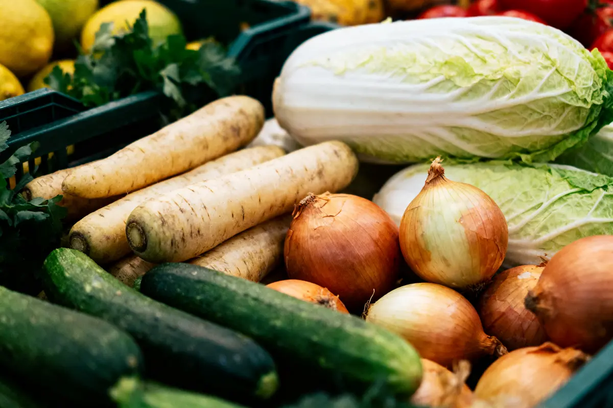 Légumes variés sur un étal : choux chinois, oignons, concombres, panais. Couleurs vives et fraîcheur apparente.