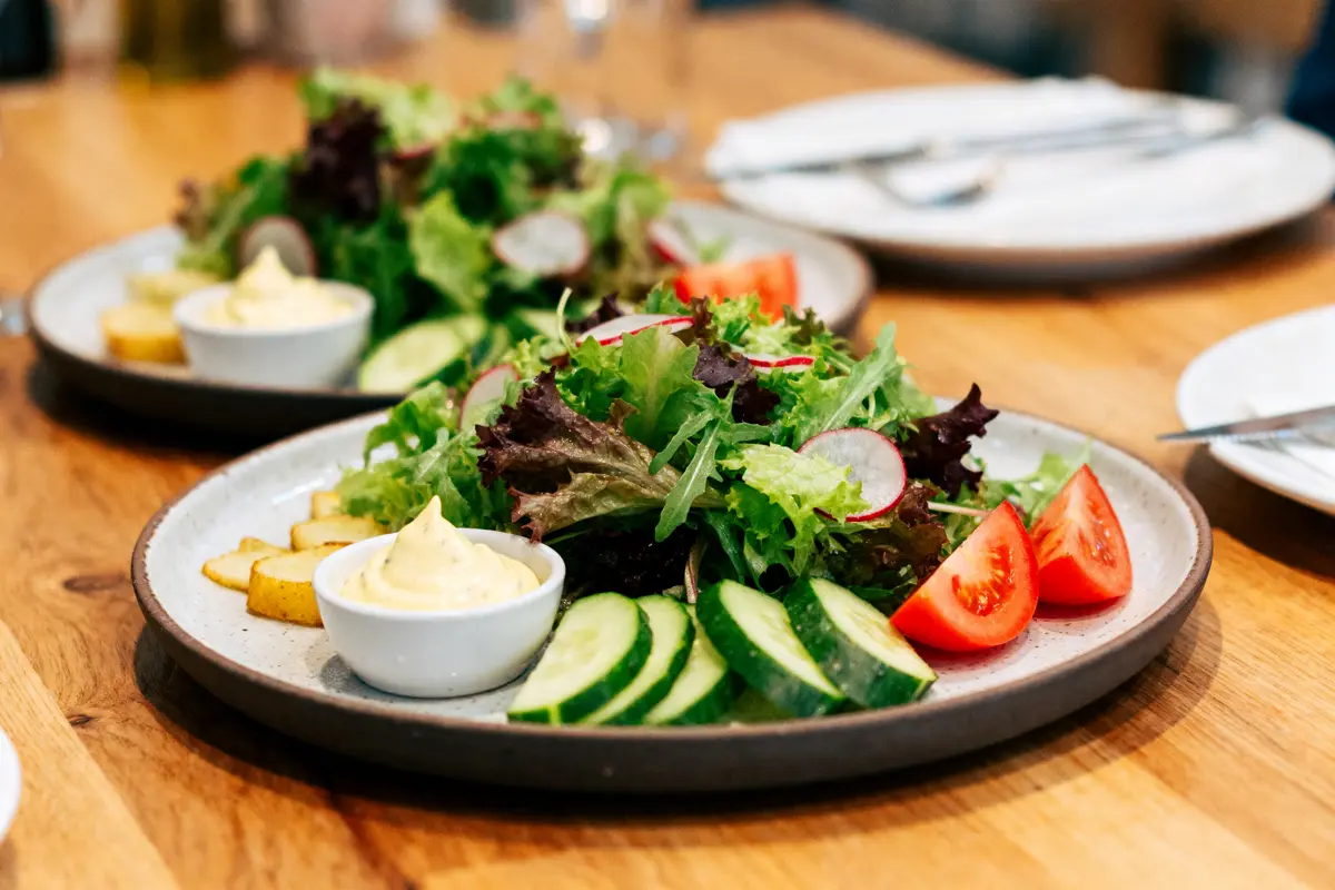 Assiette de salade fraîche avec concombres, tomates, radis, pommes de terre, et sauce mayonnaise sur table en bois.