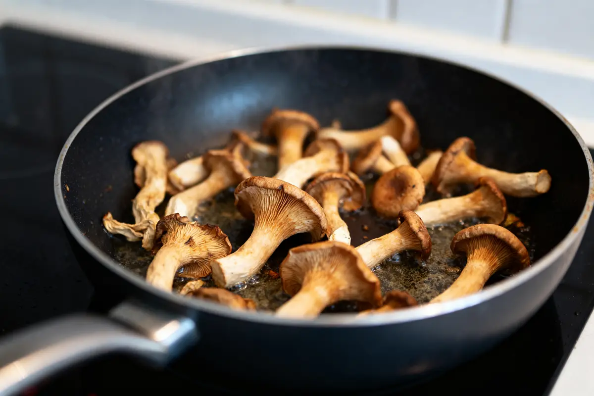 Champignons trompettes-de-la-mort cuisant dans une poêle sur une plaque de cuisson chaude
