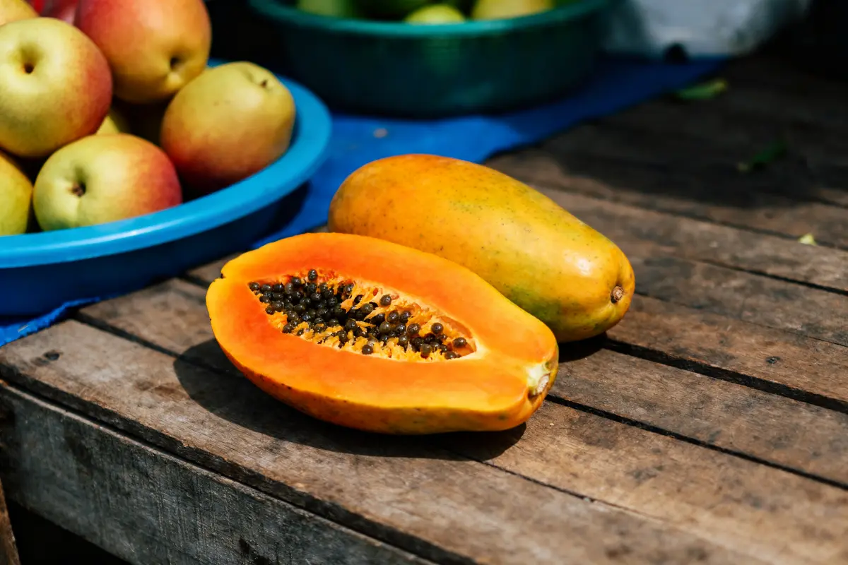 Papaye mûre coupée en deux avec graines et autres fruits exotiques orange éparpillés