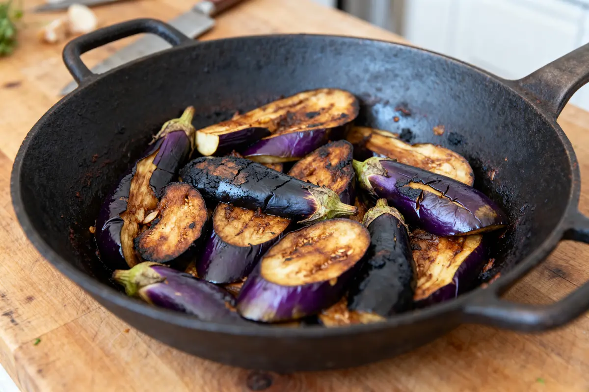 Poêlée d'aubergines grillées dans poêle en fonte sur planche en bois.