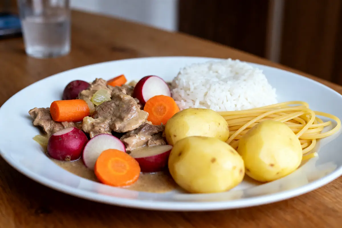Assiette de blanquette de veau avec riz, pommes de terre, pâtes et légumes variés.