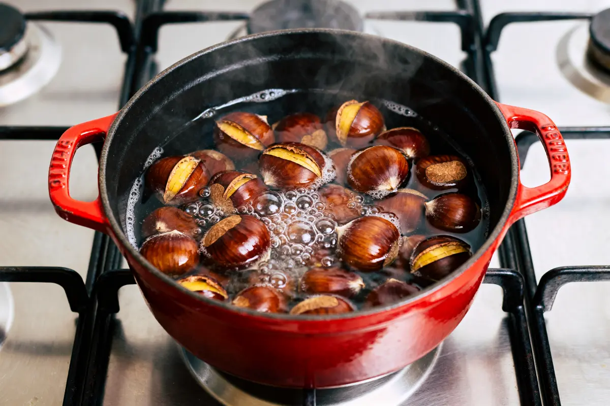 Châtaignes bouillonnant dans cocotte minute rouge pour cuisson des châtaignes à l'eau.