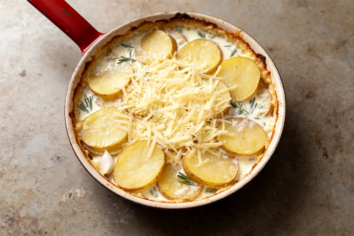 Plat de recette de gratin aux pommes de terre avec fromage râpé et herbes aromatiques