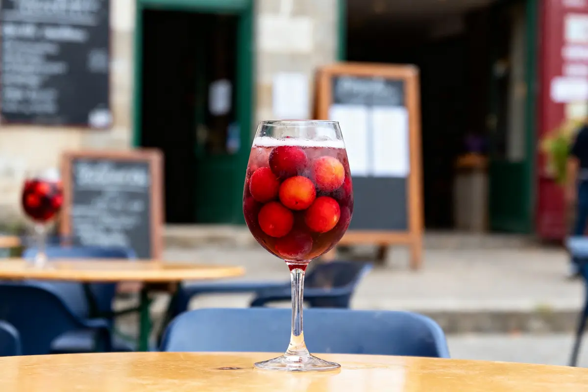 Verre de sangria aux fruits rouges sur table de café en terrasse, arrière-plan flou.
