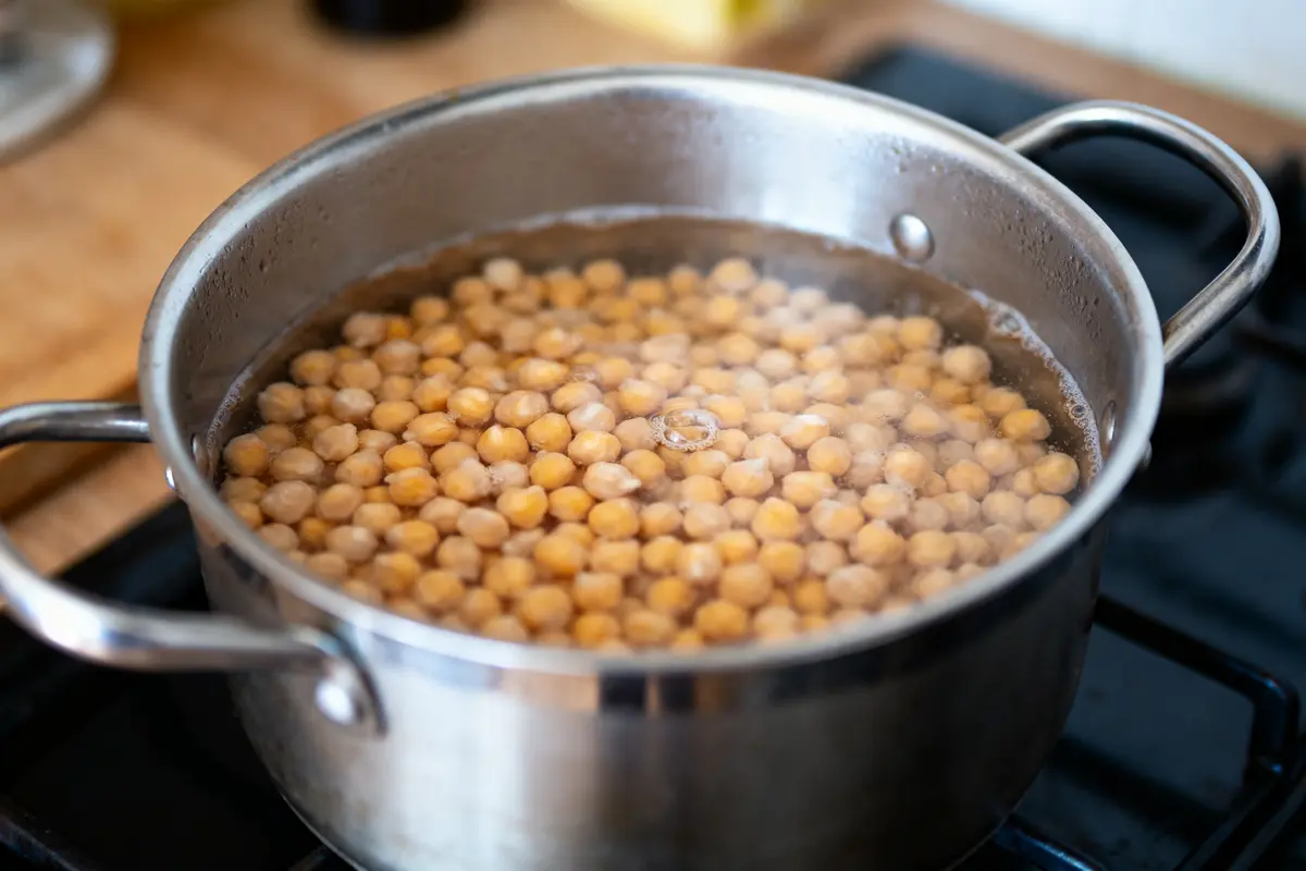 Casserole d'eau bouillante contenant des pois chiches en cuisson sur une cuisinière.